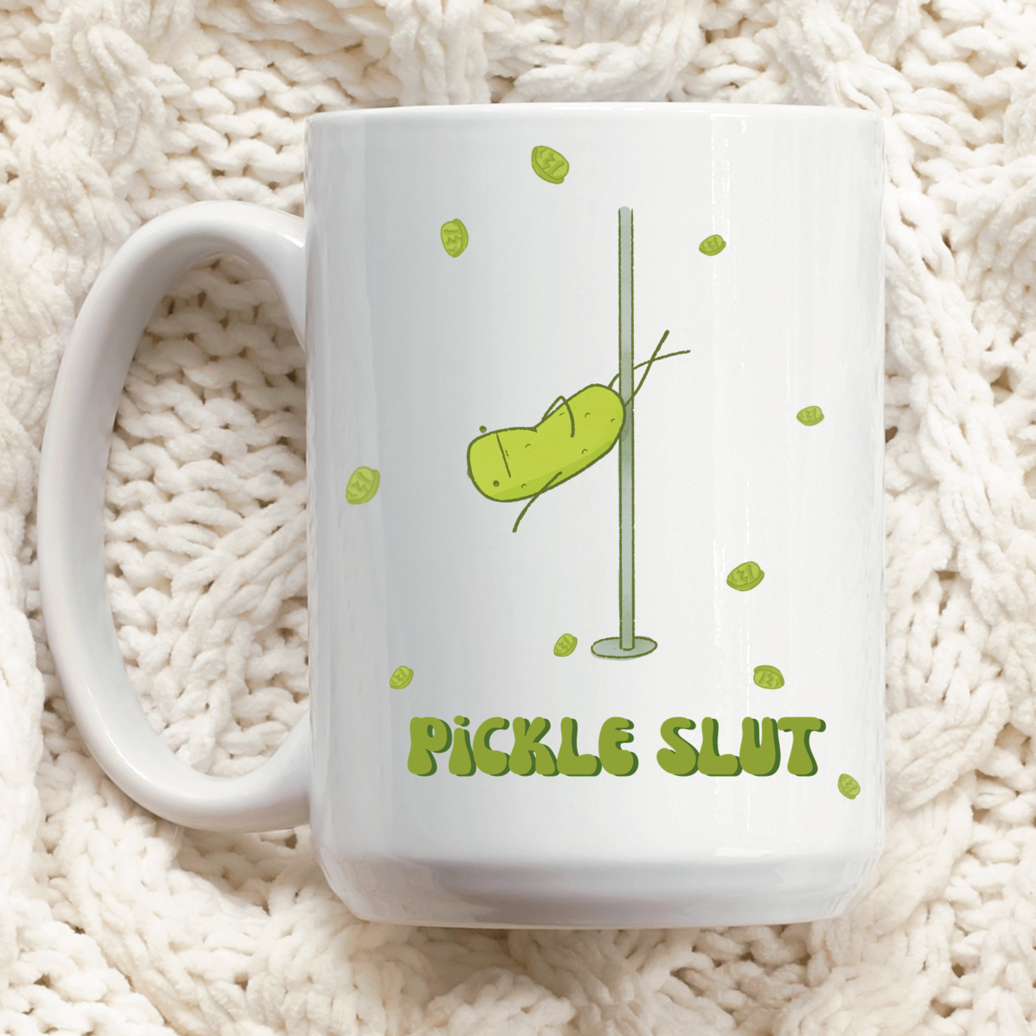a pickle mug featuring a funny illustration of a cute pickle character pole dancing for pickle chips and text that says "pickle slut" is displayed over a quilted tablecloth