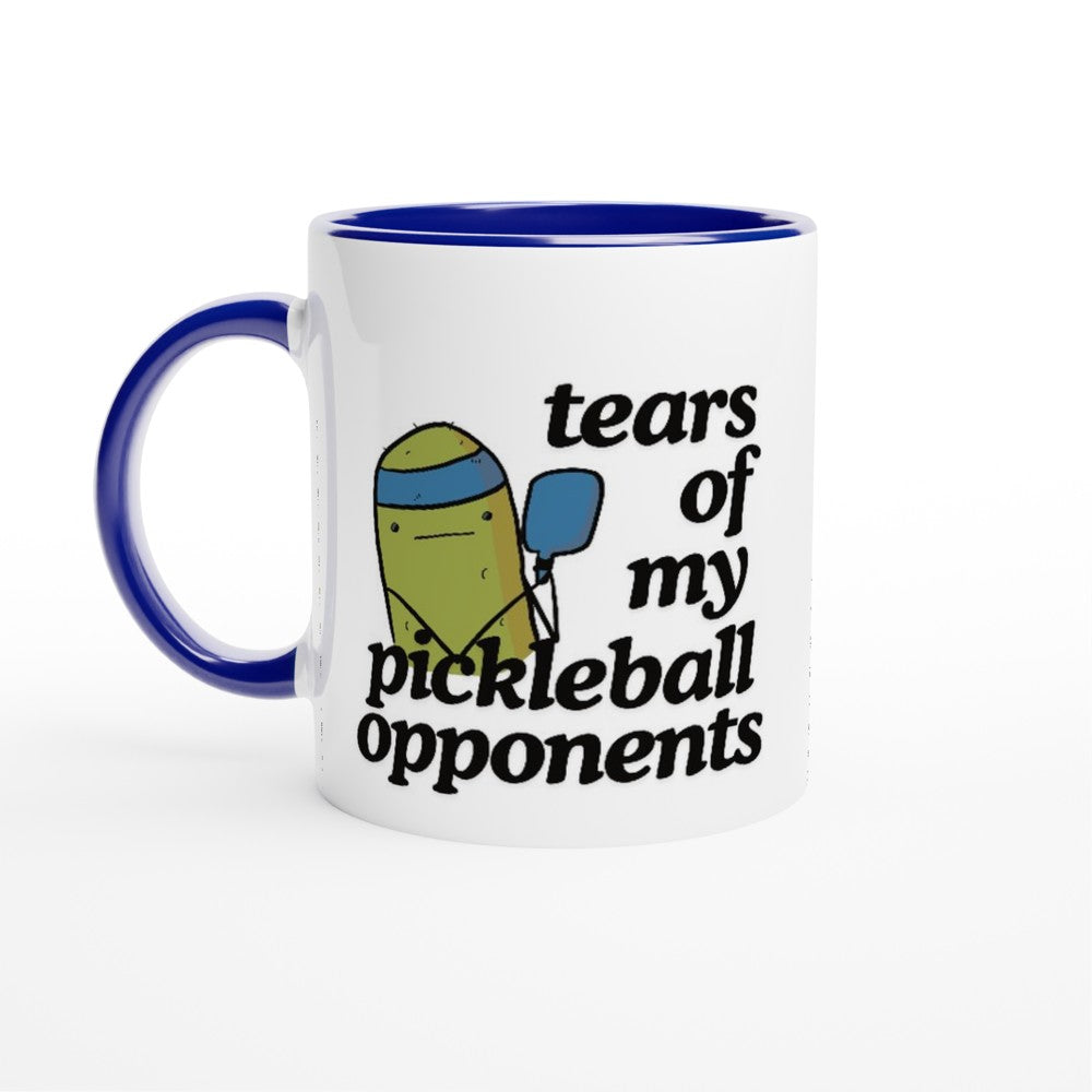 view of a pickle ball mug with a funny quote that says "tears of my pickle ball opponents" with cute illustration of a pickle holding a blue pickle ball paddle