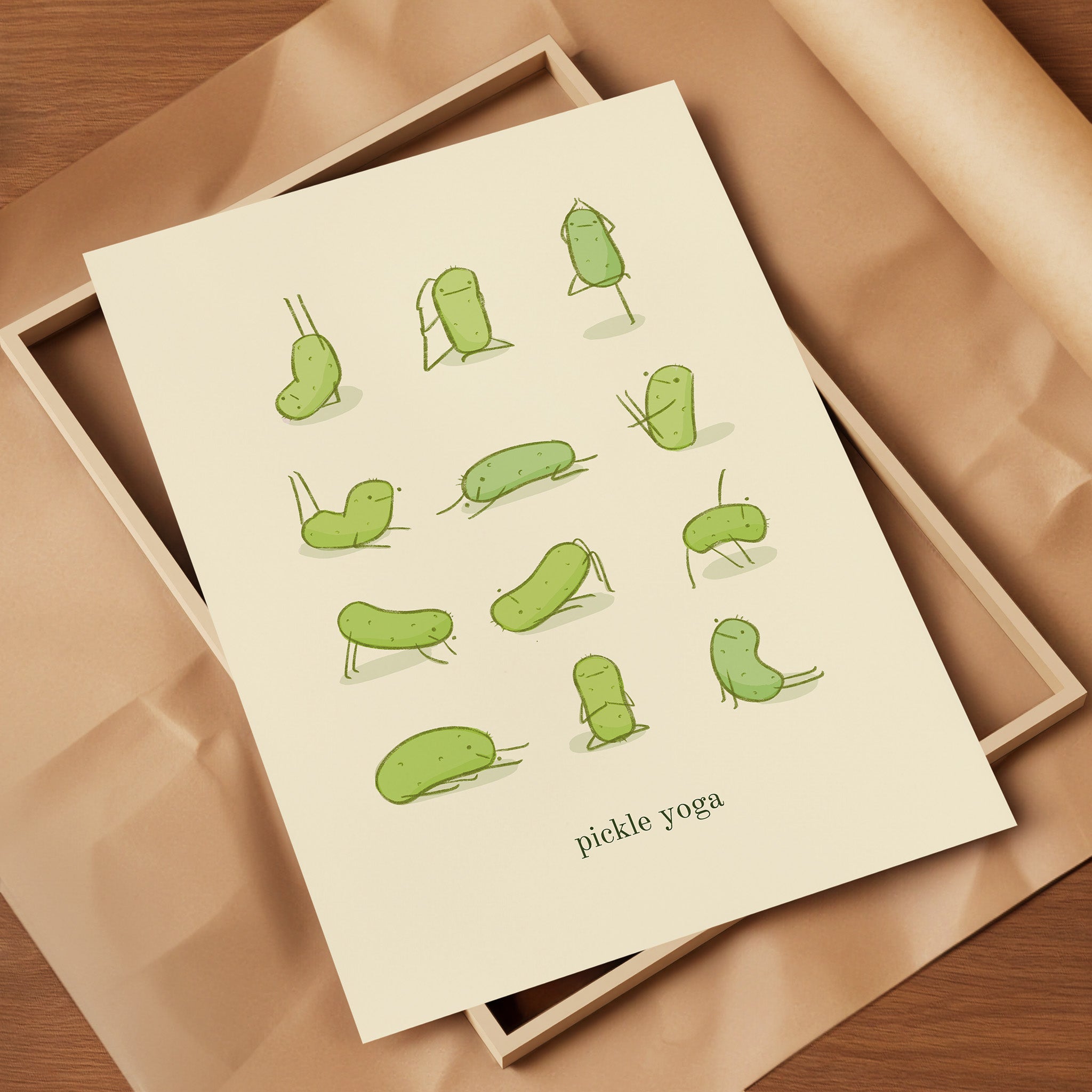 a funny pickle art print features a cute pickle in various yoga poses over text at the bottom that reads "pickle yoga" is displayed on top of packing materials