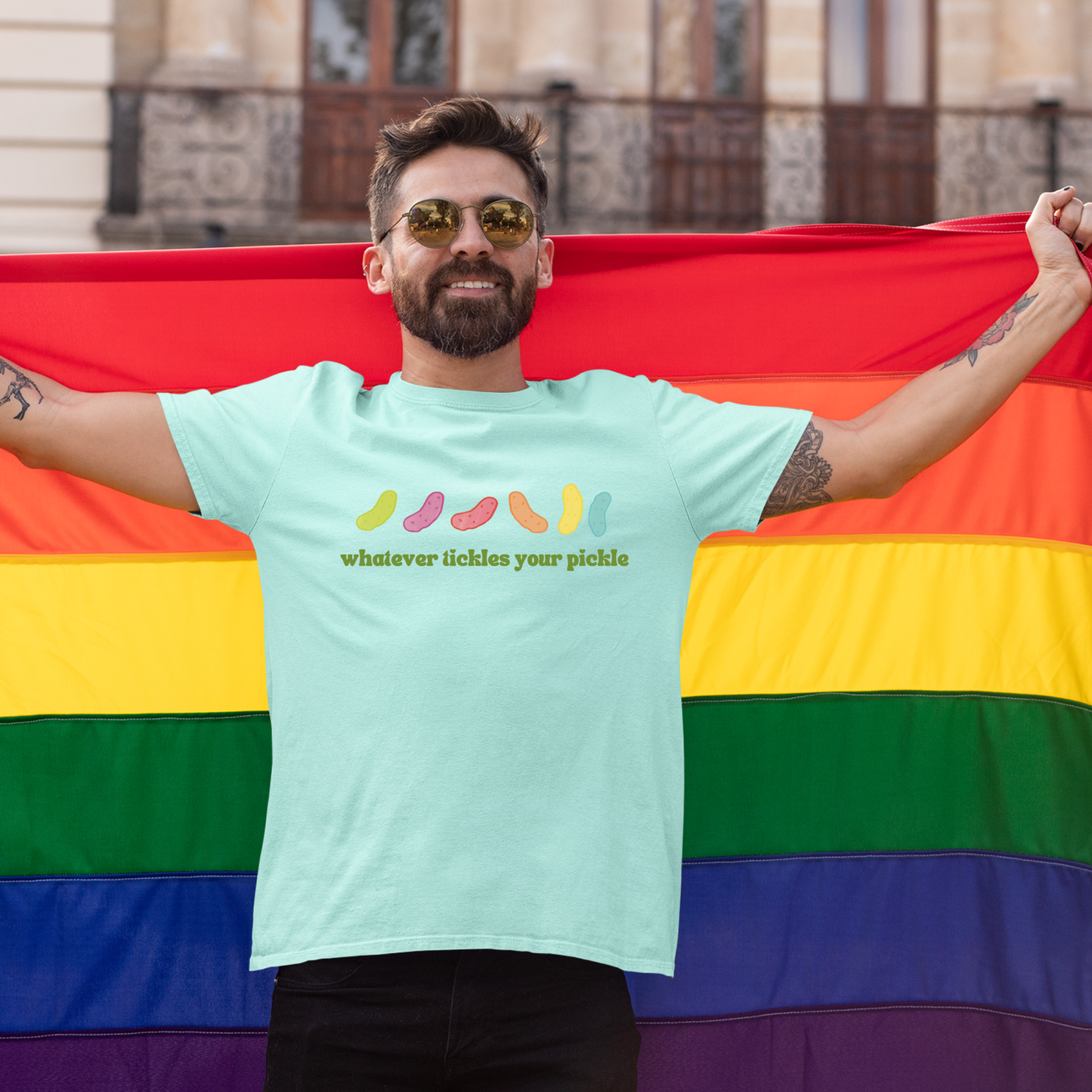 photo of a gay man wearing a pickle themed pride tshirt while holding a pride flag