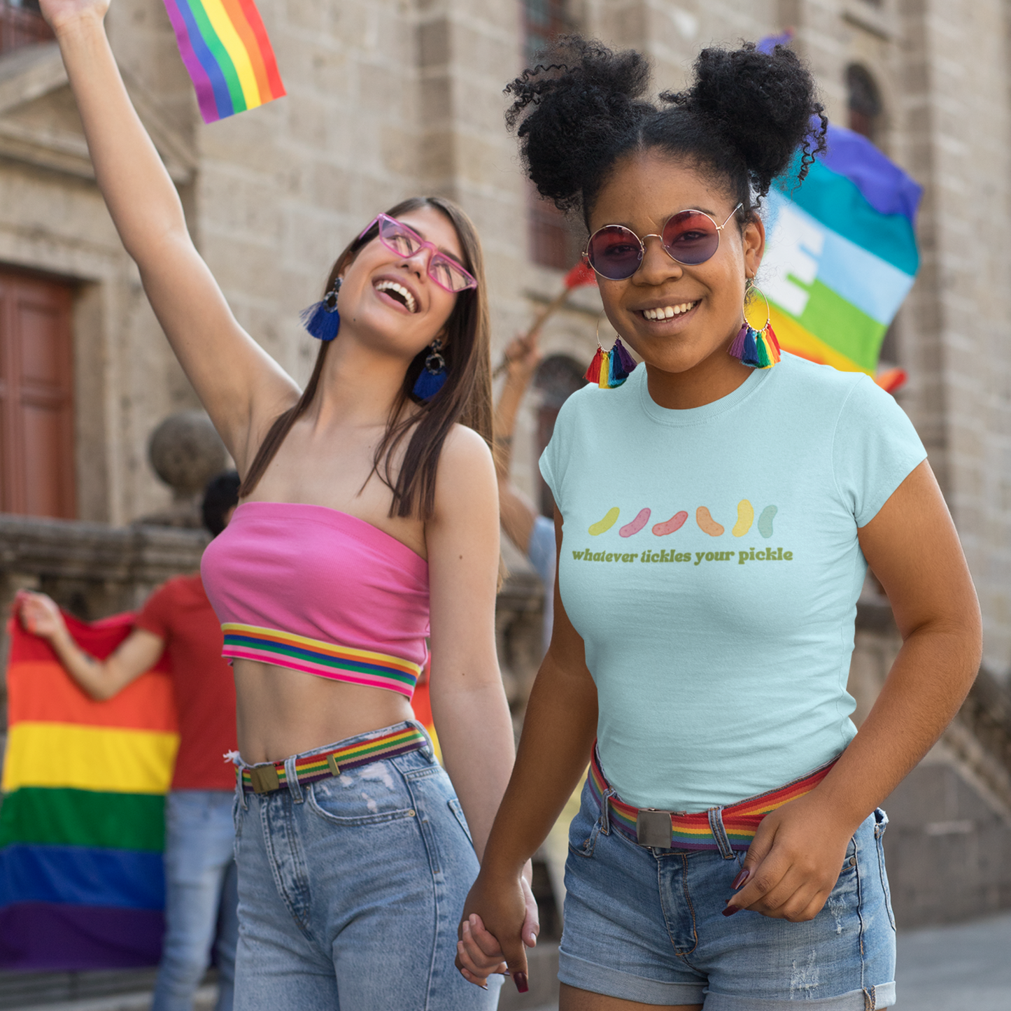 a lesbian couple at a pride event holding hands and wearing a pride tshirt that has a pride quote "whatever tickles your pickle"