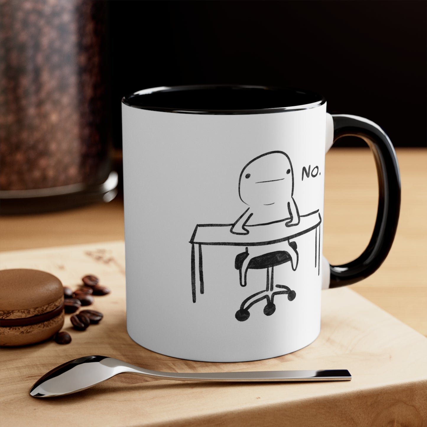 white ceramic coffee mug with black handle and funny illustration of doodle person sitting at desk with the word "no" on table with coffee beans