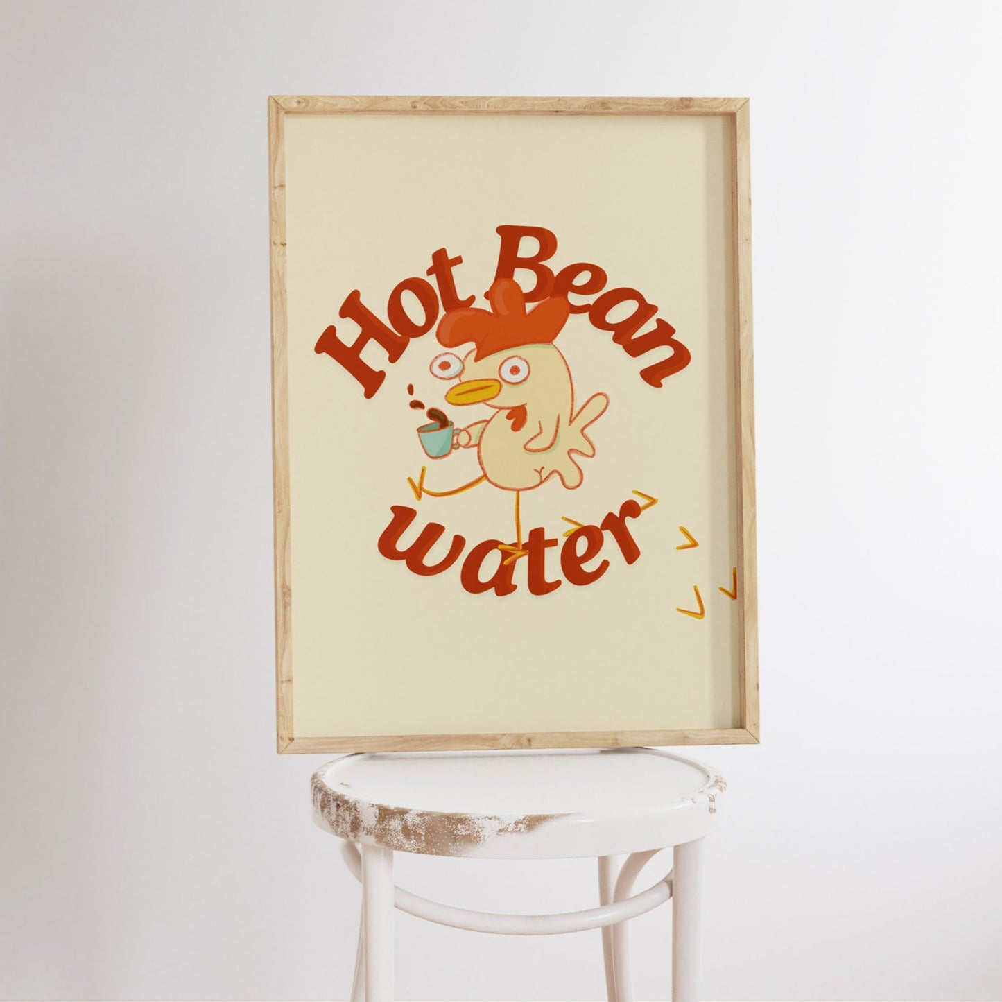 a funny coffee art print that features a chicken holding a cup of coffee next to text that reads &quot;hot bean water&quot; is framed and displayed on a stool