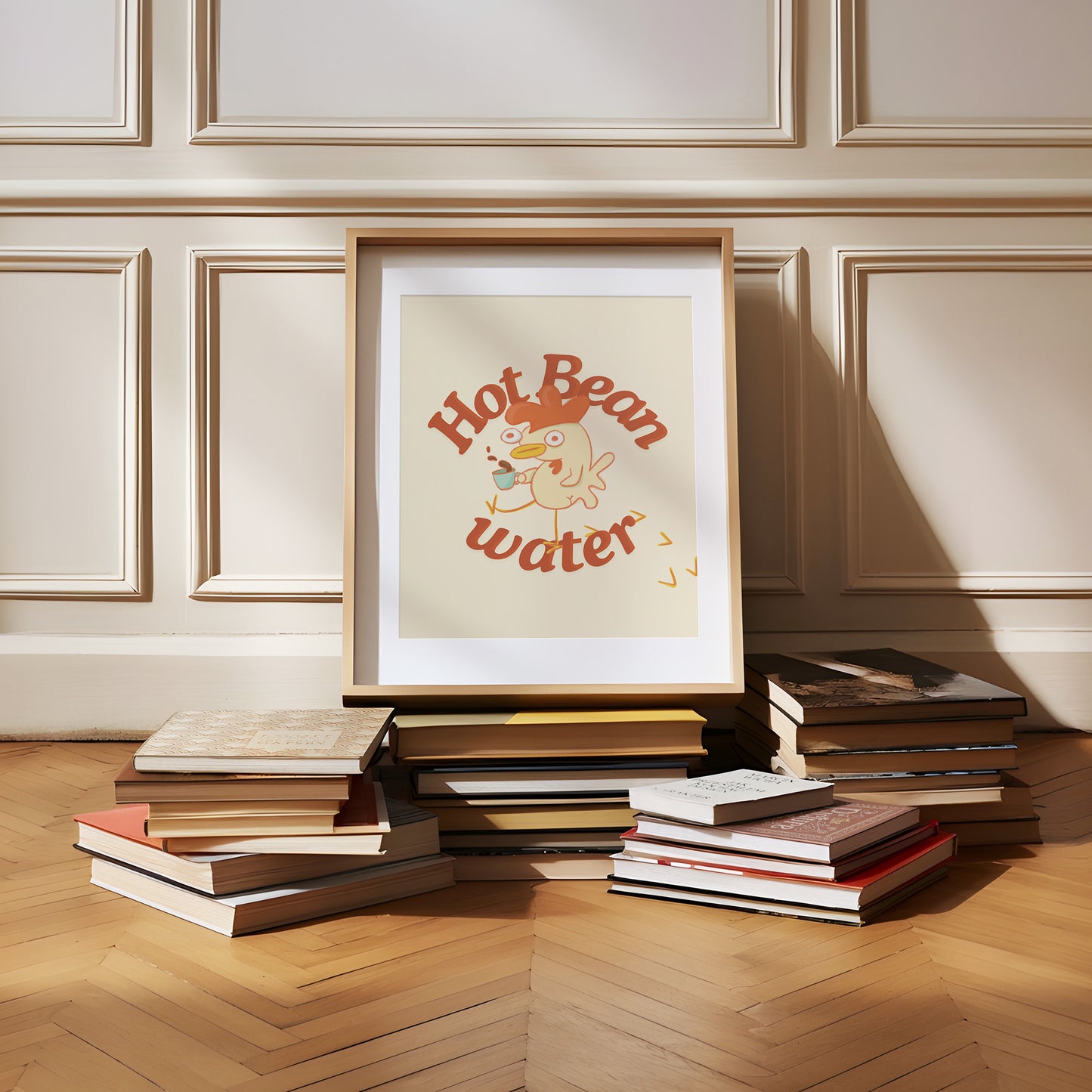 a funny coffee art print that features a chicken holding a cup of coffee next to text that reads &quot;hot bean water&quot; is framed and sitting on a pile of books