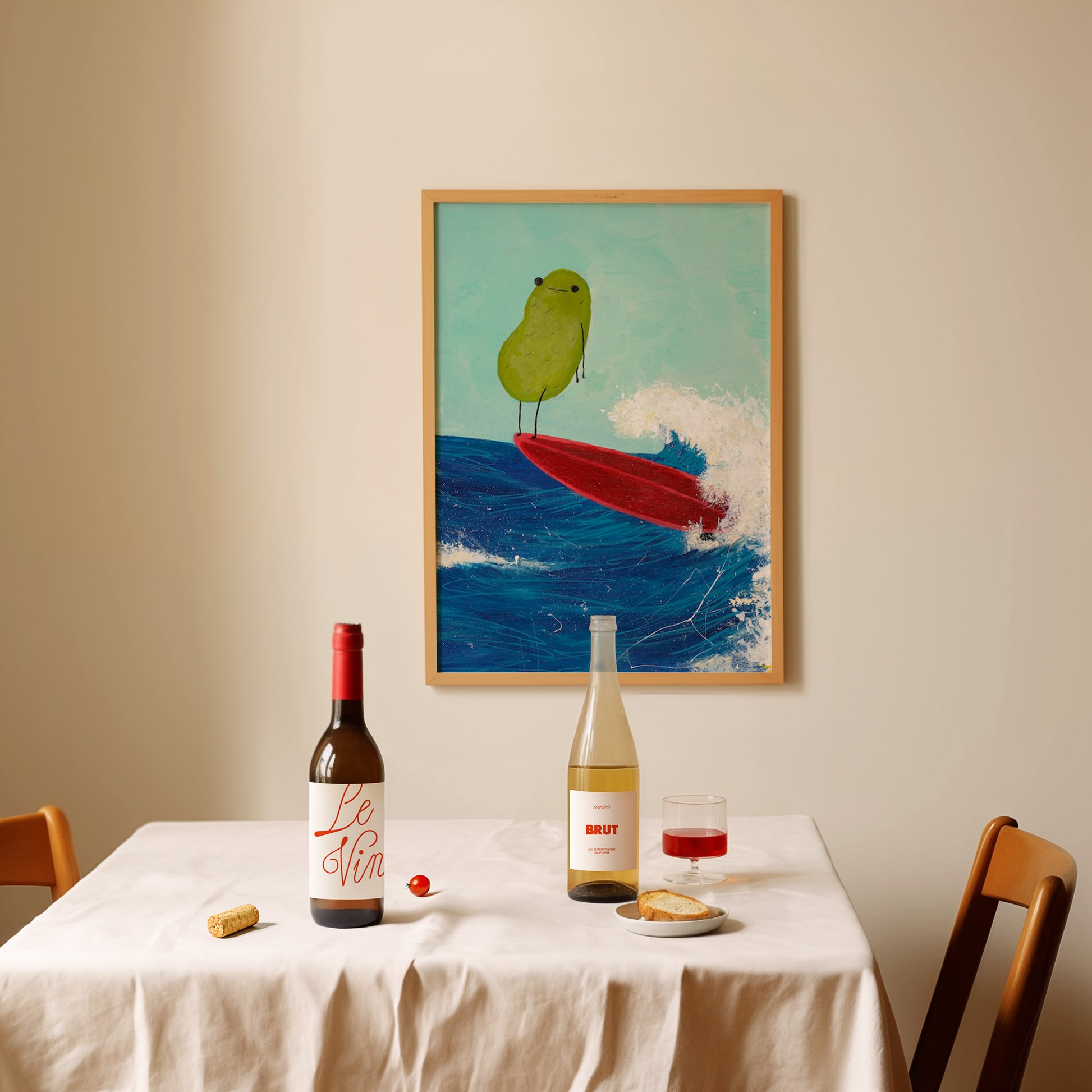 a pickle art print featuring a cute pickle riding a red surfboard on a wave is displayed over a dining room table