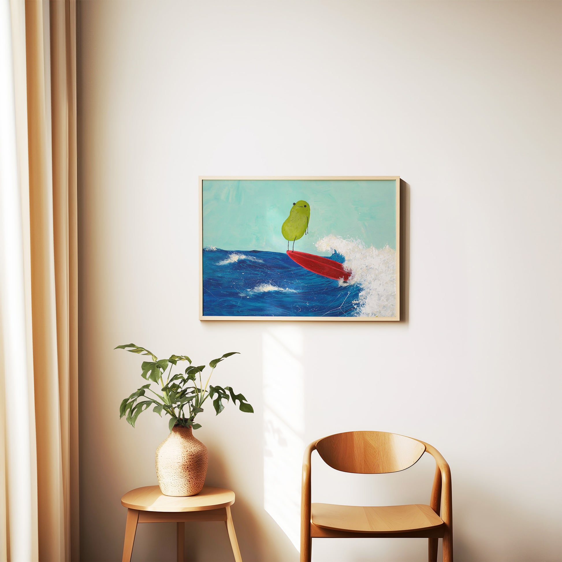 a pickle art print featuring a cute pickle riding a red surfboard on a wave is displayed in a wooden frame on a wall above a wooden chair and houseplant