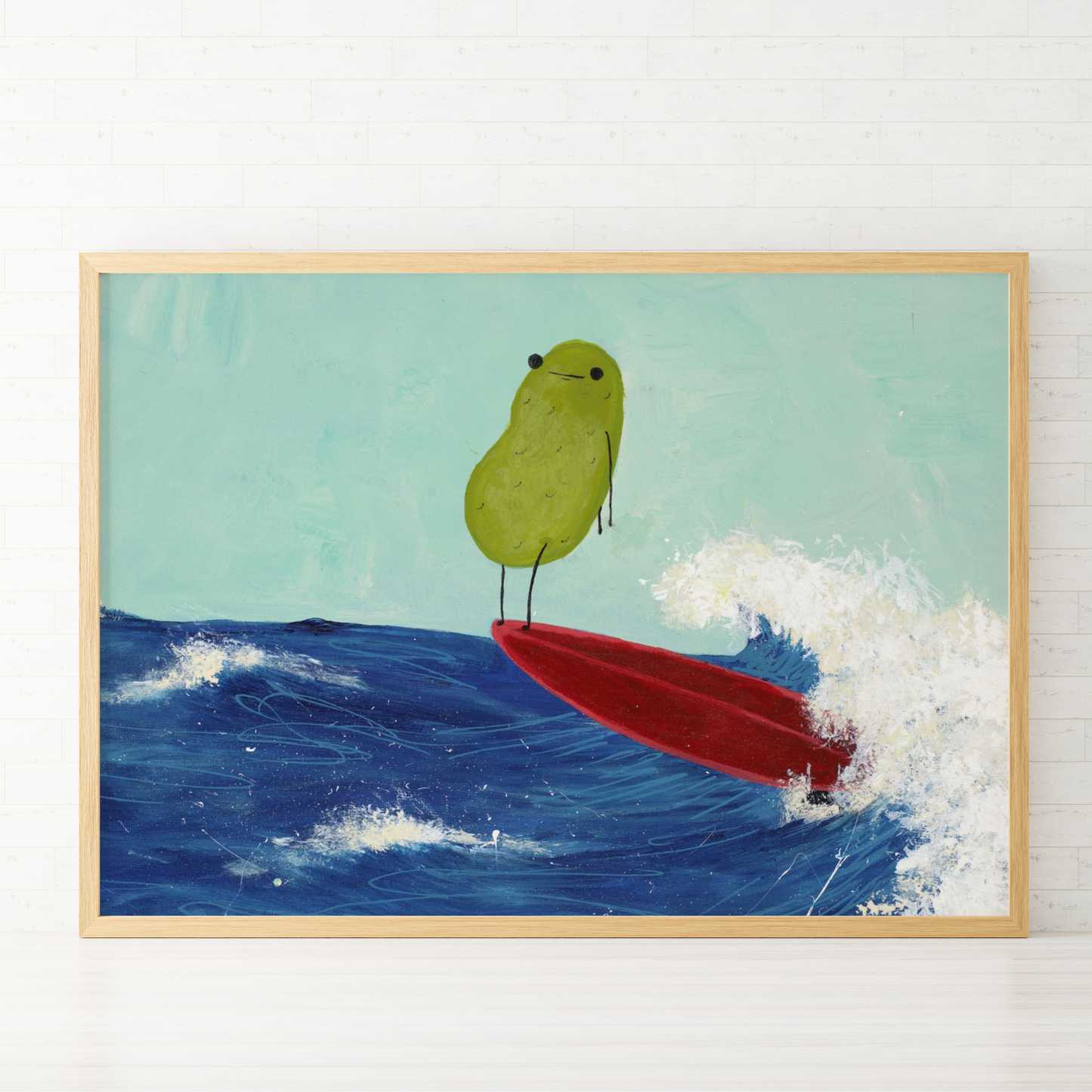 a pickle art print featuring a cute pickle riding a red surfboard on a wave is displayed in a wooden frame against a white tiled wall