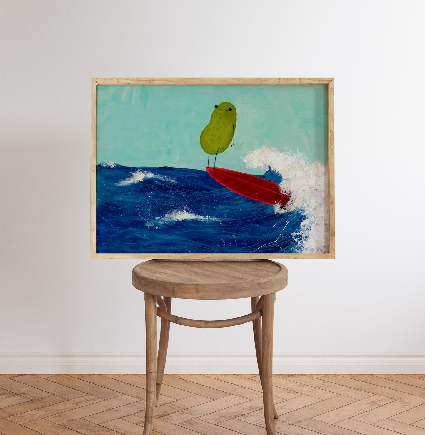 a pickle art print featuring a cute pickle riding a red surfboard on a wave is displayed in a wooden frame that is mounted on a kitchen chair