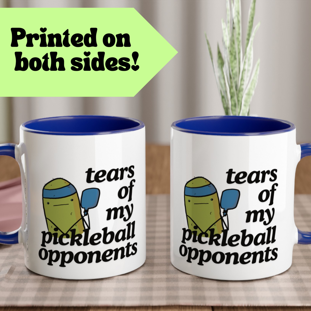 view of a pickle ball mug with a funny quote that says "tears of my pickle ball opponents" with cute illustration of a pickle holding a blue pickle ball paddle