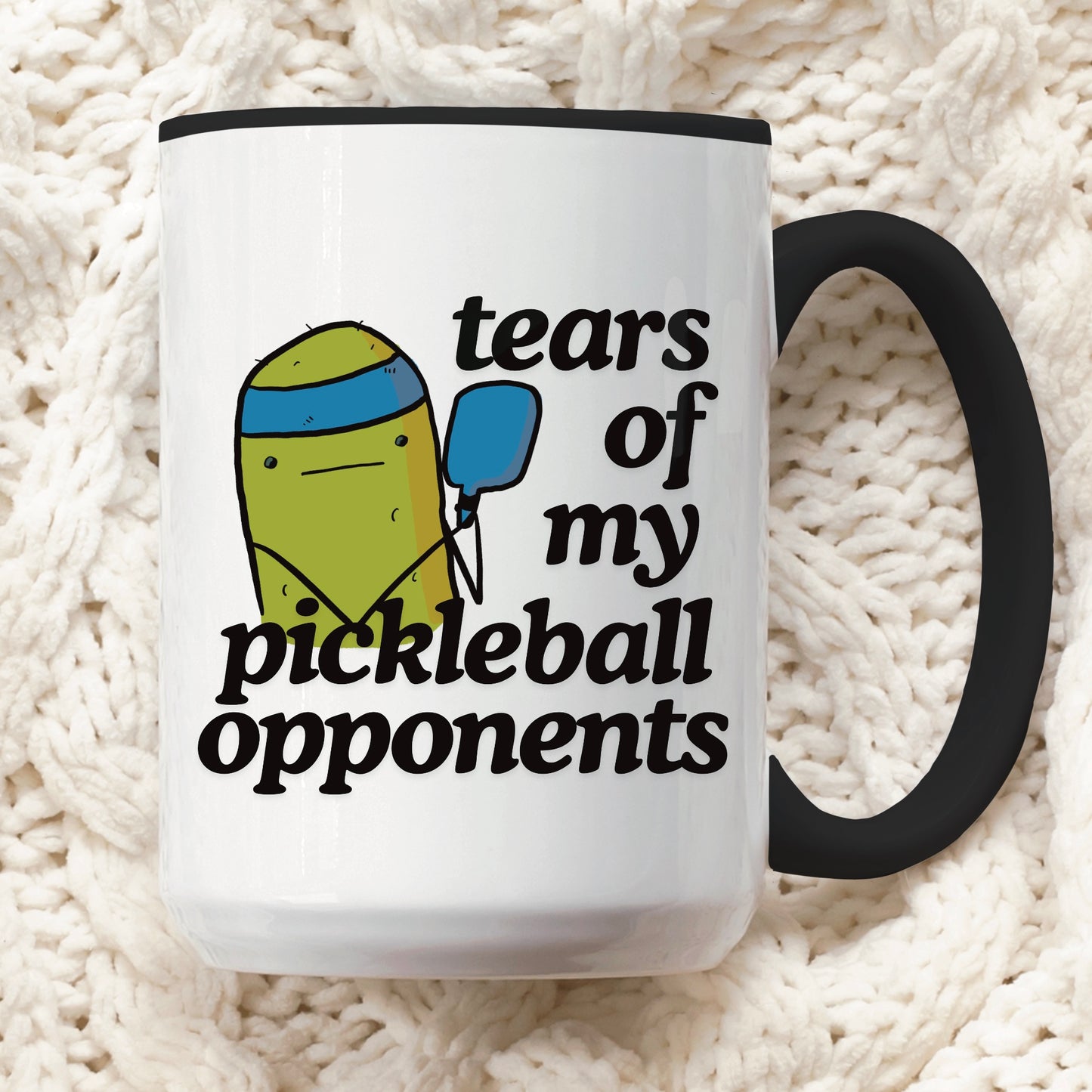 view of a pickleball mug with a quote that says "tears of my pickleball opponents" with cute illustration of a pickle holding a blue pickleball paddle