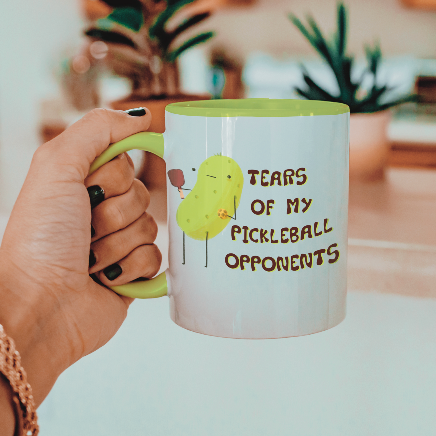 image of a hand holding a pickleball mug with funny quote that says "tears of my pickleball opponents" next to illustration of a pickle holding a pickleball and paddle