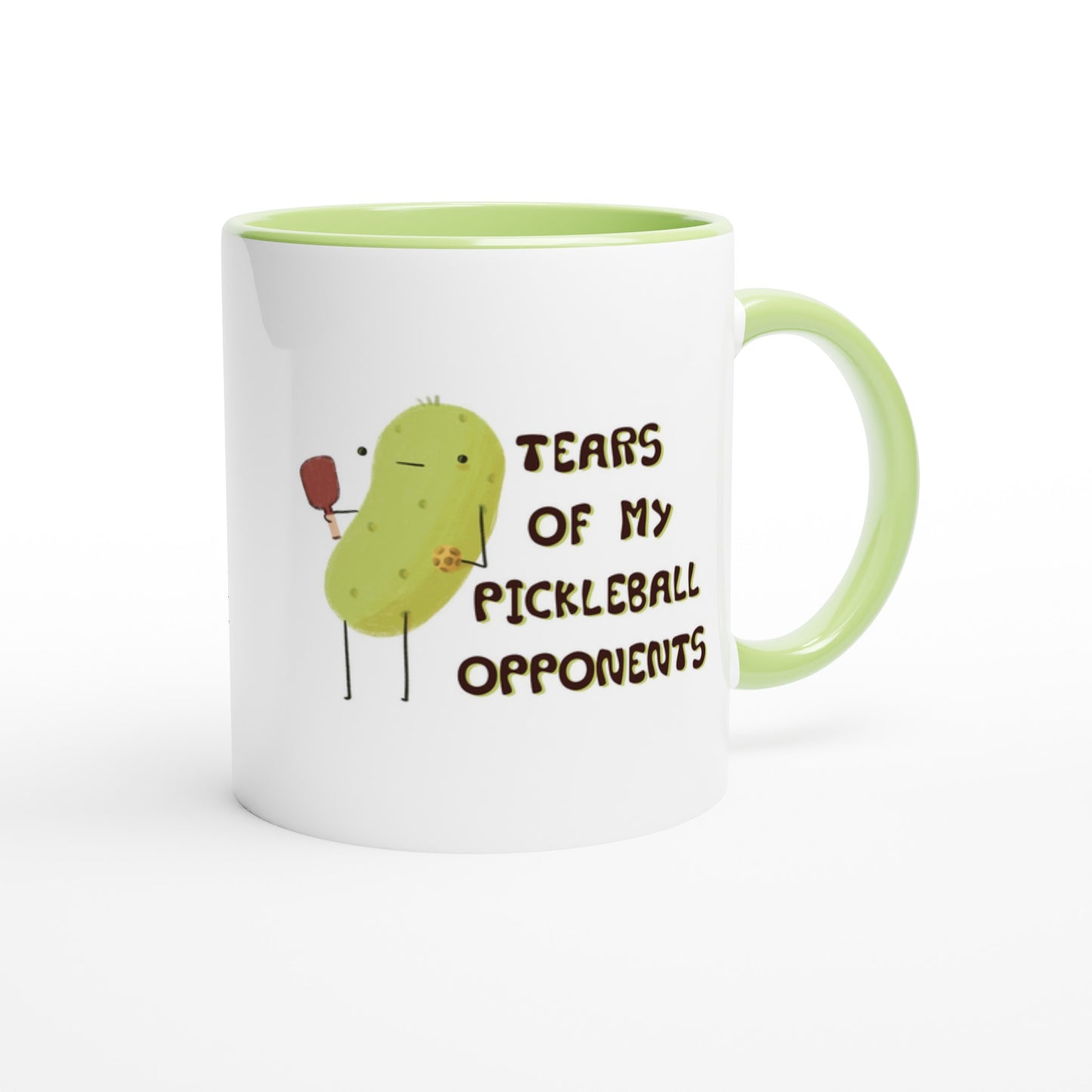 front left view of a pickleball mug with funny quote that says "tears of my pickleball opponents" next to illustration of a pickle holding a pickleball and paddle