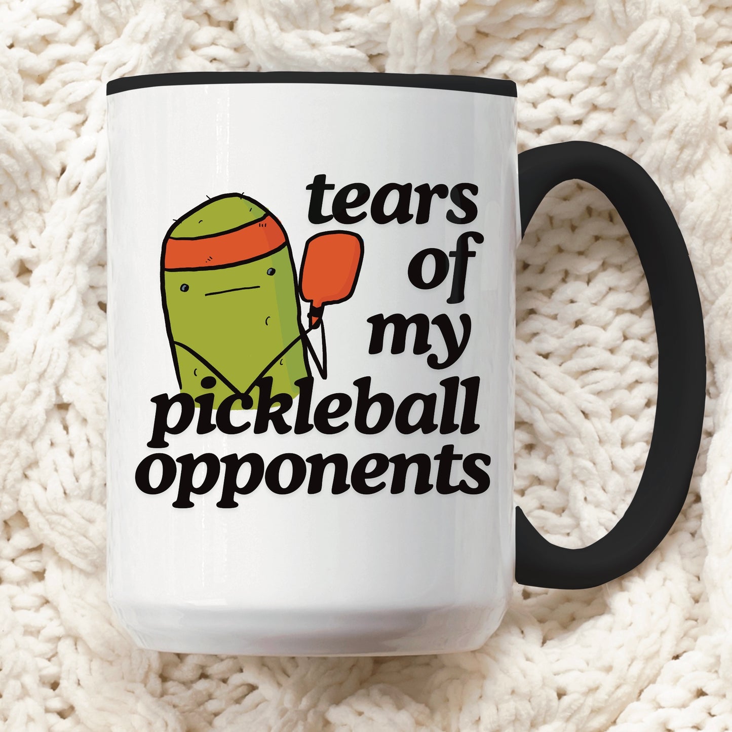 close up view of a pickleball mug with a quote that says "tears of my pickleball opponents" with cute illustration of a pickle holding a red pickleball paddle