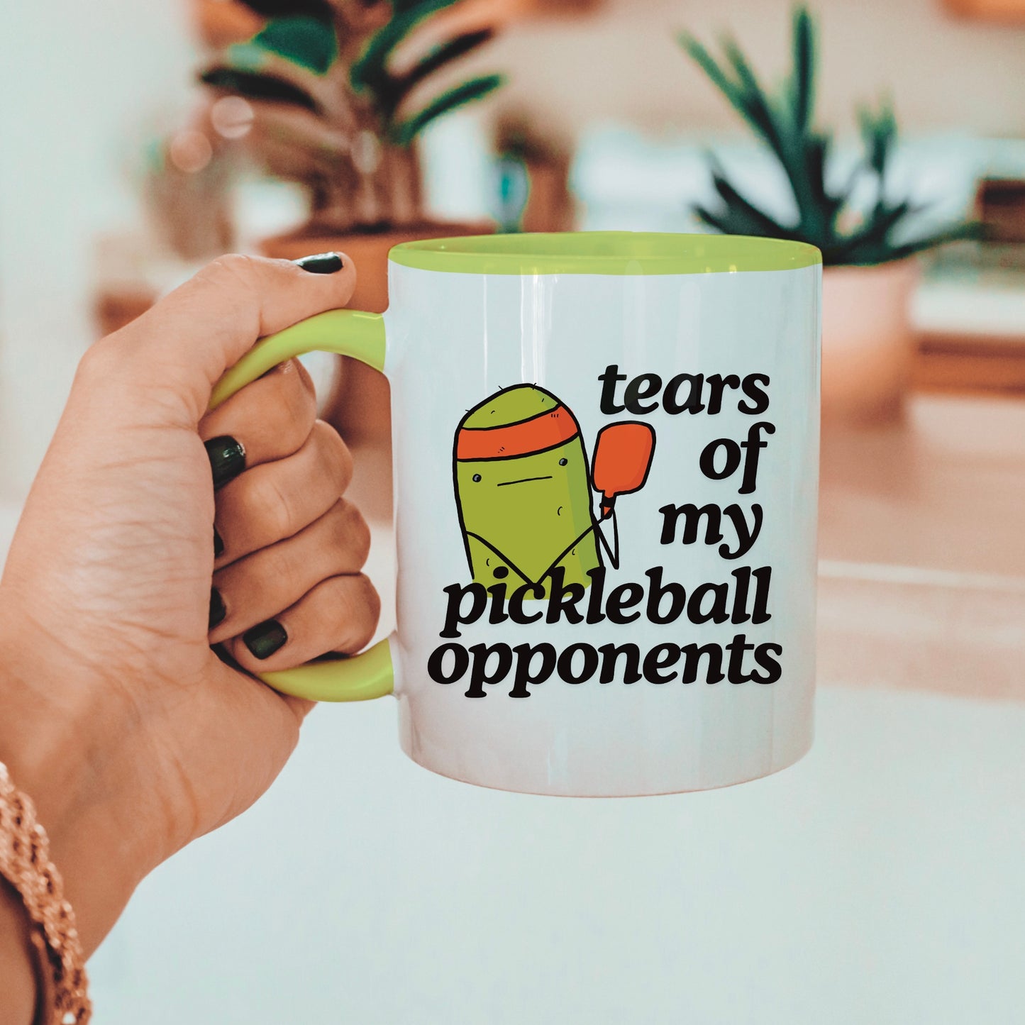 view of person holding a pickleball mug with a quote that says "tears of my pickleball opponents" with cute illustration of a pickle holding a red pickleball paddle