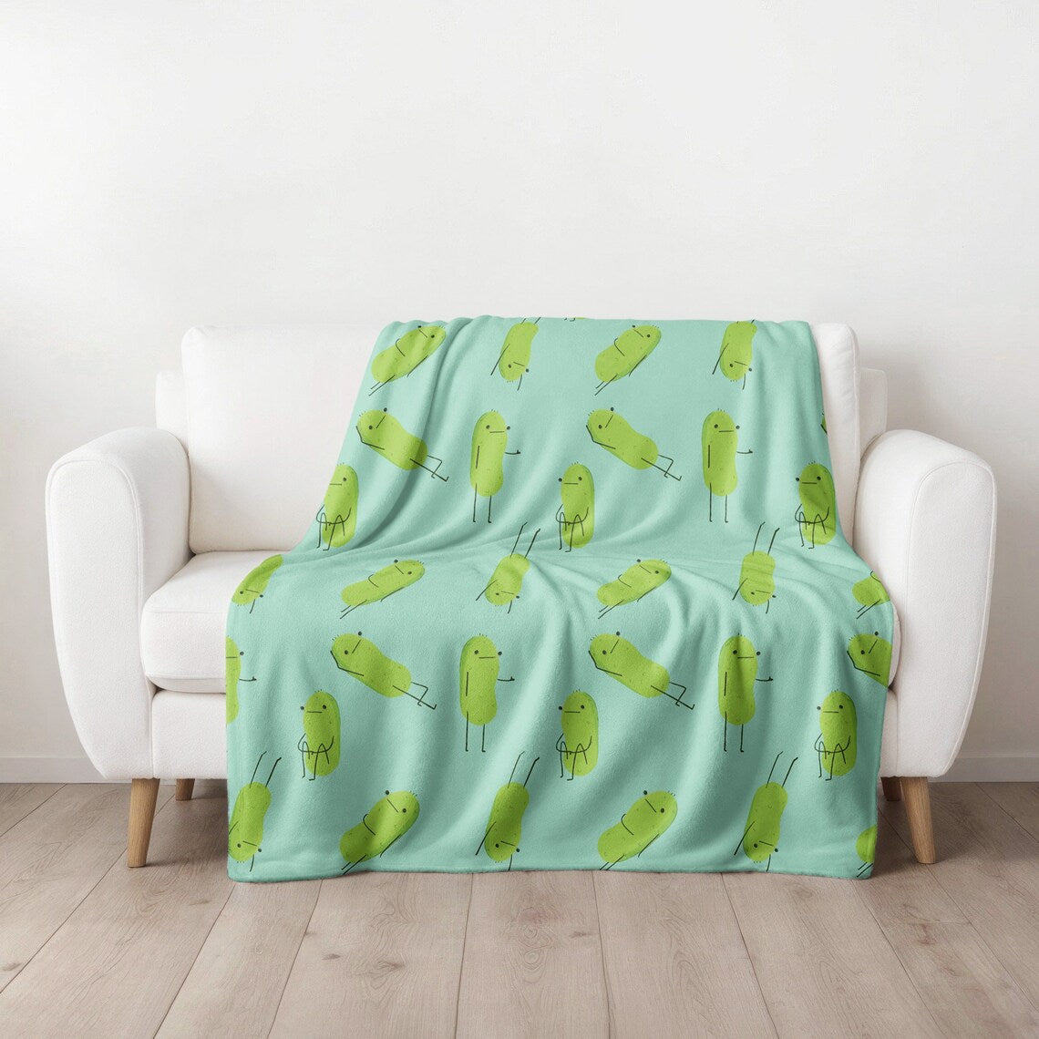 a pickle blanket that is light blue in color and has a print pattern of cute pickle characters in different positions is draped over a white couch