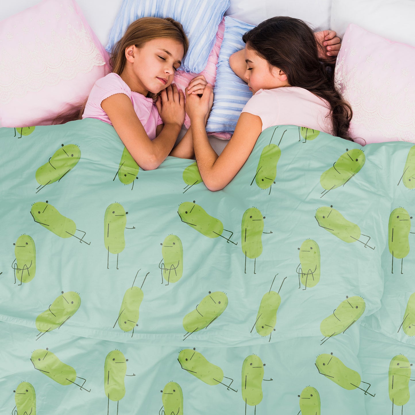 a pickle blanket that is light blue in color and has a print pattern of cute pickle characters in different positions is displayed on a bed with two sleeping children sibling under it